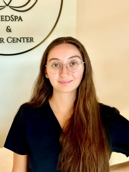Jillian Almstead, licensed esthetician and electrologist, standing beneath the River City Aesthetics lotus logo on the studio wall