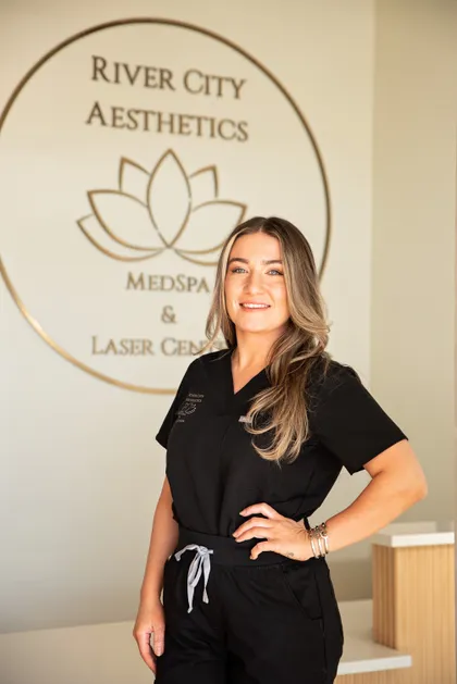Kendall Regan, licensed esthetician and certified laser specialist, in front of the River City Aesthetics studio wall