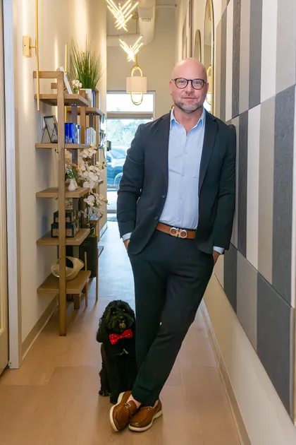 Michael Spagna, owner of River City Aesthetics, standing in the studio hallway with Kevin the dog at his feet